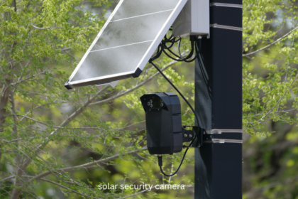 Solar security camera with solar panel mounted on a black pole with green trees in the background