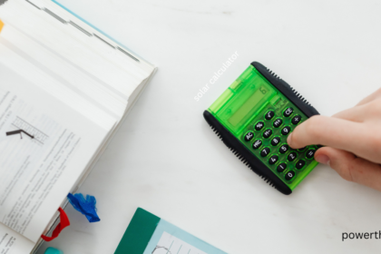 Person using a green solar calculator on a desk with an open textbook to estimate solar panel output
