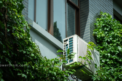 A modern outdoor air source heat pump unit mounted on a building wall surrounded by green vines, professionally set up by air source heat pump installers.