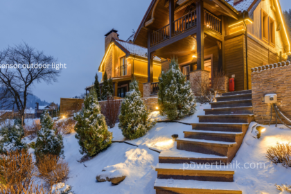 Motion sensor outdoor light illuminating snowy stone steps and a wooden chalet at dusk, with warm LED lights outlining the roof