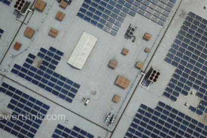 Aerial top-down view showing a massive array of solar panels on a flat roof of an industrial facility.