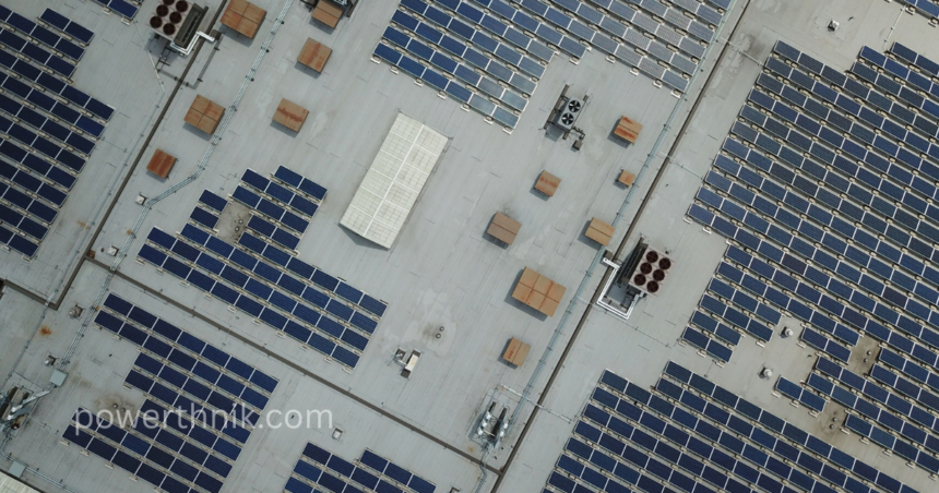 Aerial top-down view showing a massive array of solar panels on a flat roof of an industrial facility.