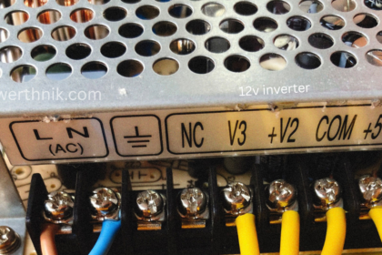 12v inverter power supply terminal block showing AC input L N, ground, and NC, V3, +V2, COM, +5V output connections with yellow wires.