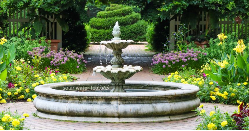 Solar water feature three-tier stone fountain in a circular basin surrounded by yellow marigolds and purple alliums in a brick-paved garden.